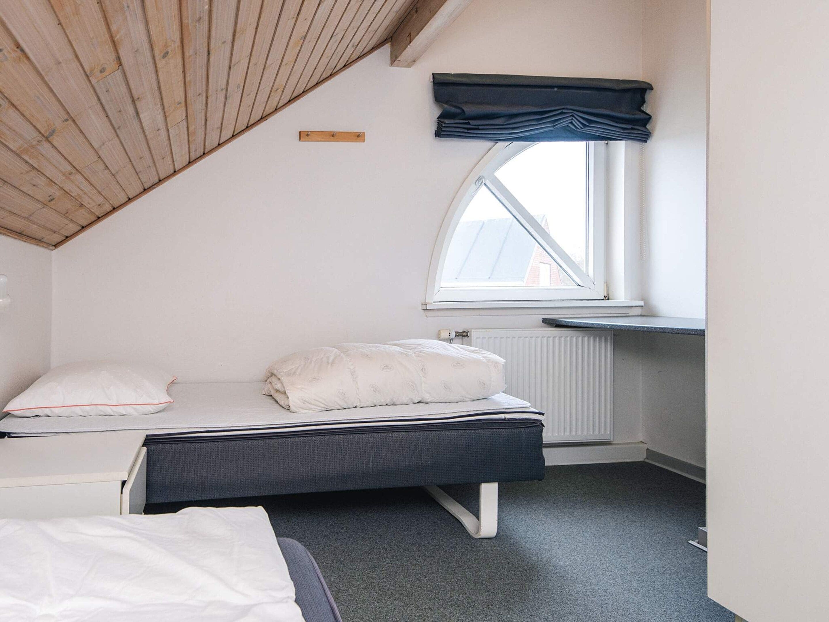 A bedroom with a sloped ceiling, a bed with a dark headboard, a window with a view, and a radiator.