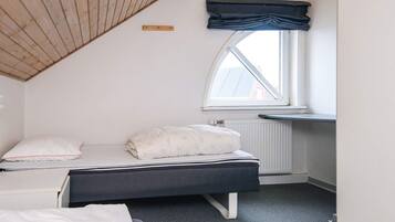 A bedroom with a sloped ceiling, a bed with a dark headboard, a window with a view, and a radiator.