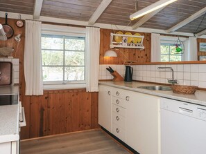 Una cocina con paredes de madera, una ventana con cortinas, un lavabo y un lavavajillas.