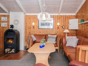 A cozy living room with a fireplace, leather sofas, a wooden table, and a wooden-paneled wall.
