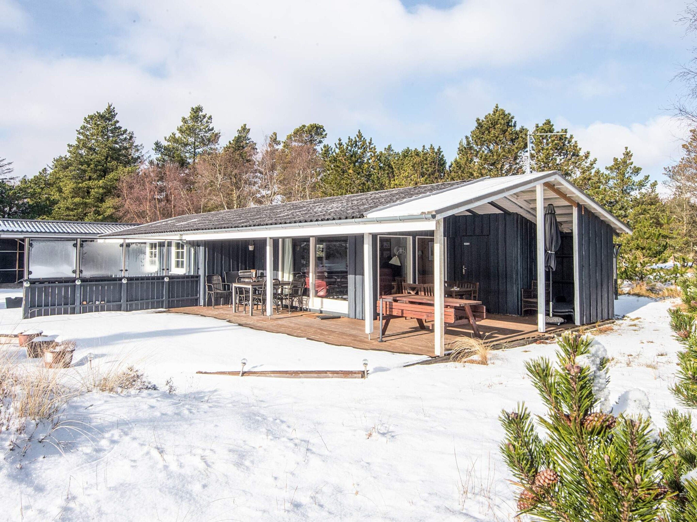 Une cabane dotée d’un patio couvert, d’une terrasse et d’une grande fenêtre donnant sur un paysage enneigé.