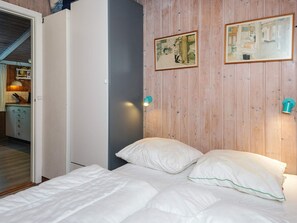 A bedroom with a bed, two wall-mounted light fixtures, and two framed pictures on the wall.