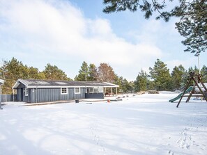 A snow-covered outdoor area with a building, a swing set, and a covered seating area.