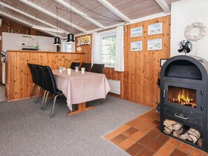 Un coin repas avec une table dressée pour quatre personnes, un poêle à bois et une cuisine en arrière-plan.
