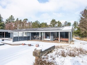 A modern house with a covered patio, outdoor seating, and a snow-covered yard.