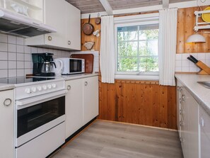 A kitchen with white cabinets, a stove, a microwave, and a window with curtains.