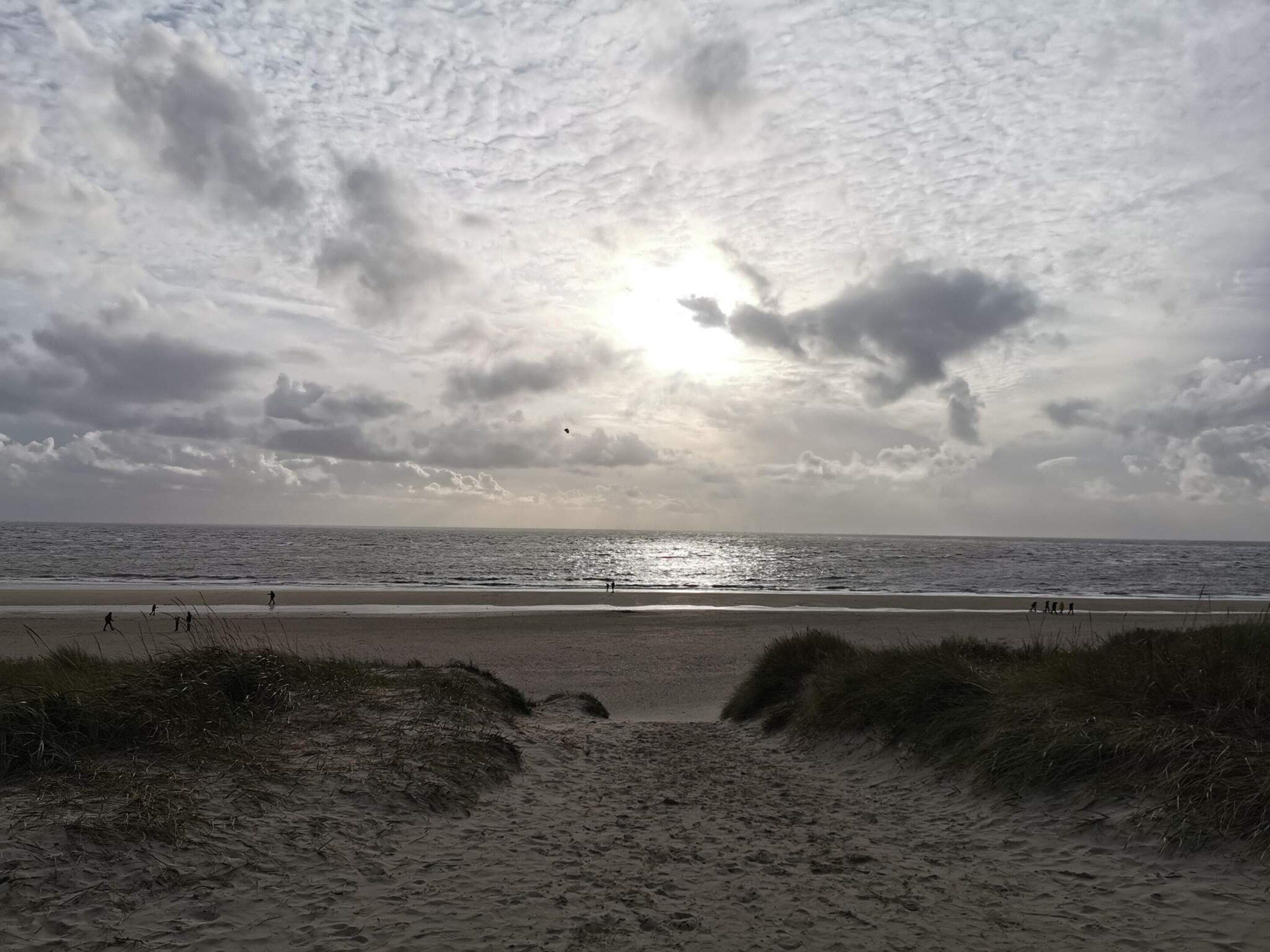 A beach with a sandy path leading to the water, under a cloudy sky.