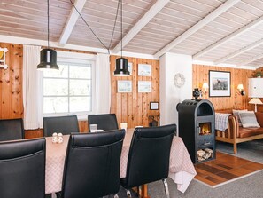 A cozy room with a wooden ceiling, a fireplace, a dining table with chairs, and a sofa.