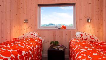 A room with two beds, a window, a small table with magazines, and a plant.
