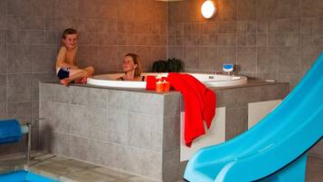 A swimming pool with a blue slide, a jacuzzi area, and a tiled wall.