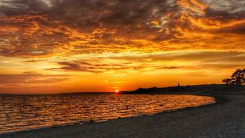 A sunset over a beach with a calm sea and a silhouette of a tree line in the distance.