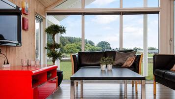 Ein modernes Wohnzimmer mit Holzboden, einer roten Unterhaltungseinheit, einem schwarzen Ledersofa, einem Couchtisch mit Glasplatte und einem großen Fenster mit Blick ins Freie.