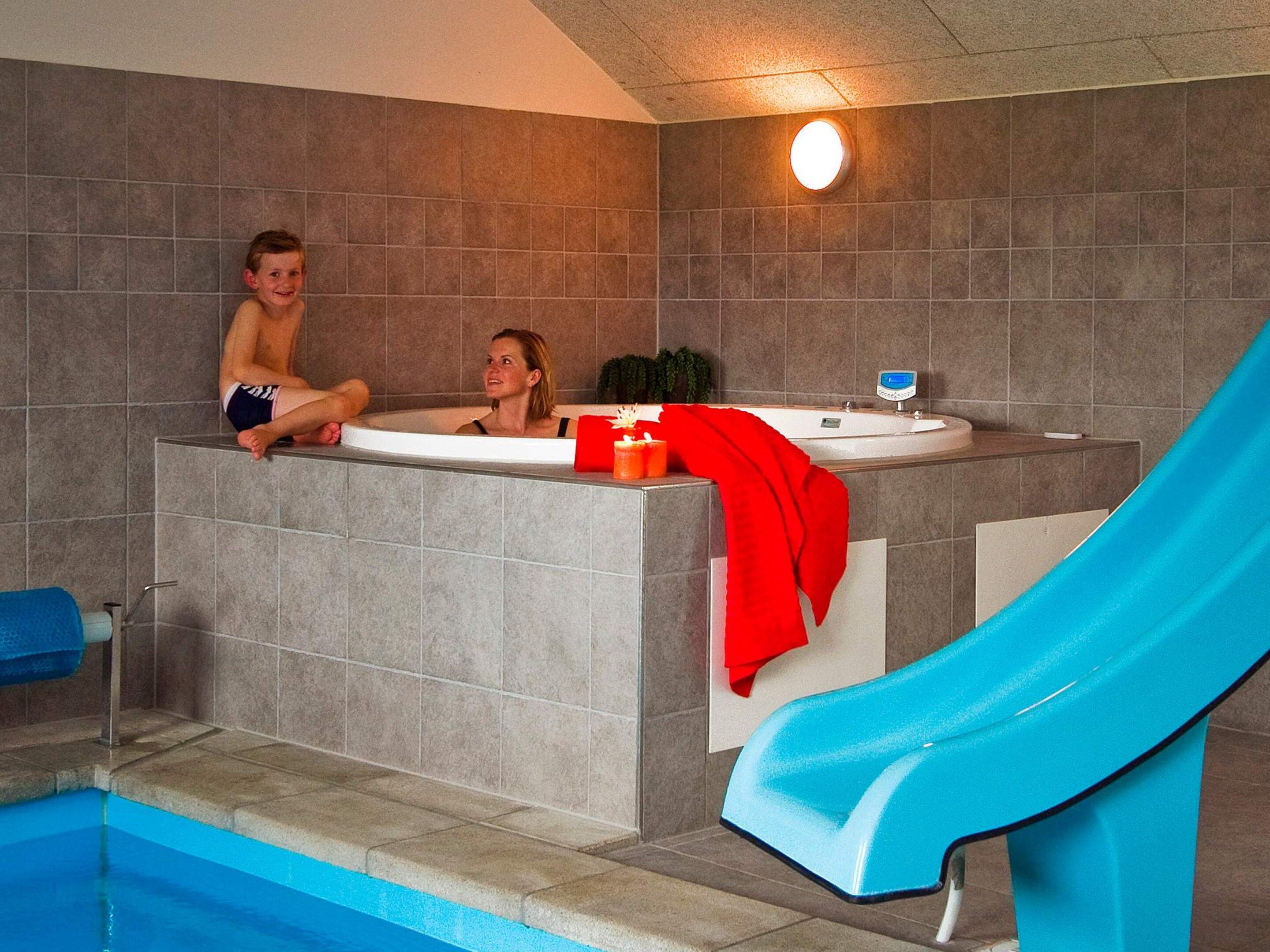 A swimming pool with a blue slide, a jacuzzi, and a person sitting on the edge of the jacuzzi.