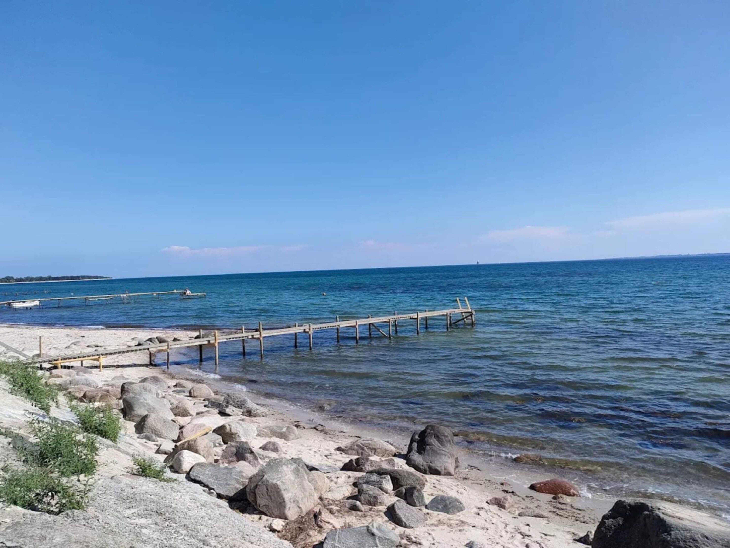 A rocky beach with a wooden pier extending into calm waters.