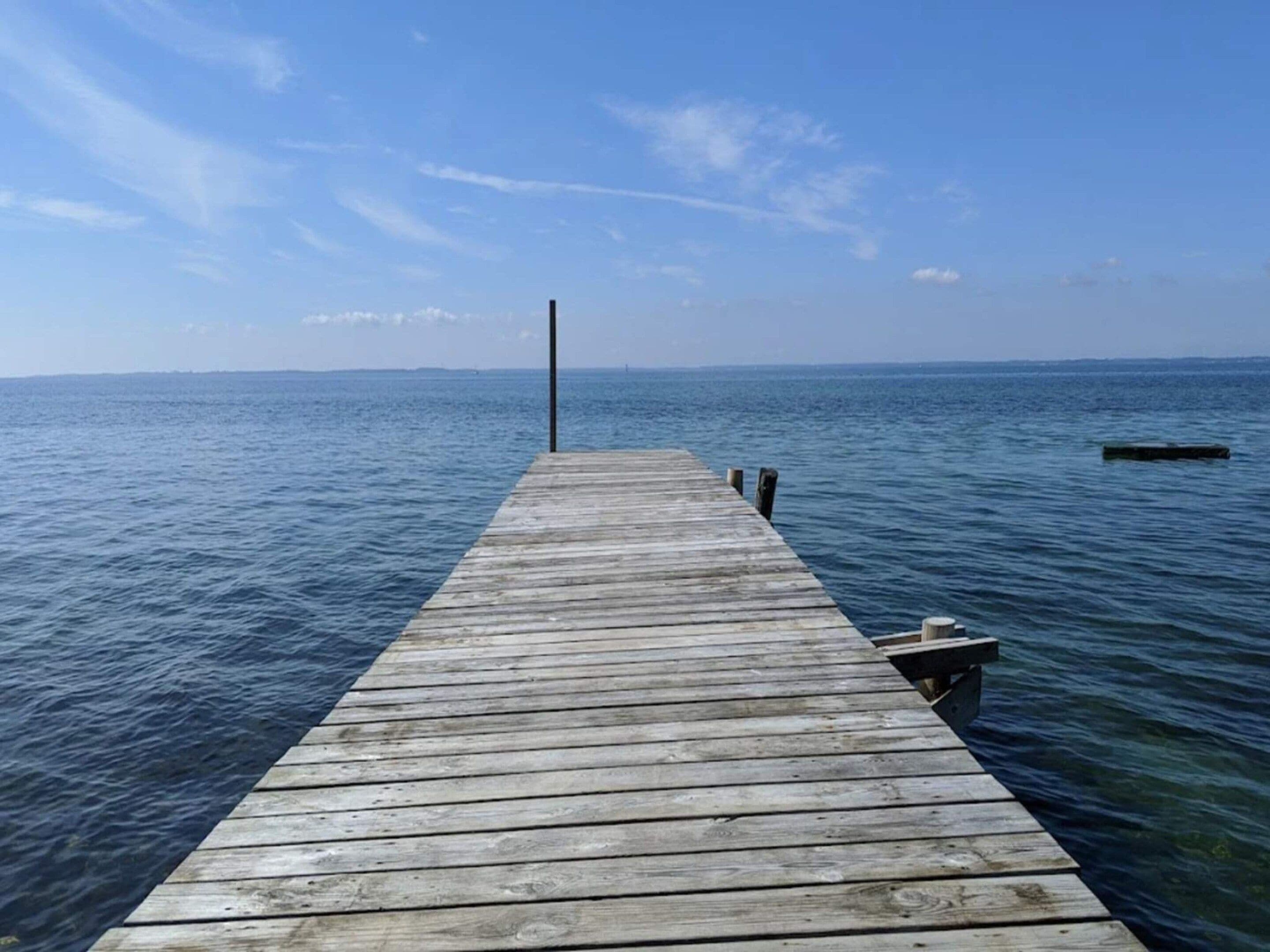 A wooden pier extending into calm water under a clear sky.
