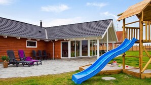 A backyard with a wooden playhouse, a slide, outdoor seating, and a covered patio area. - 5 Star Holiday Home in Sydals (Sydals)