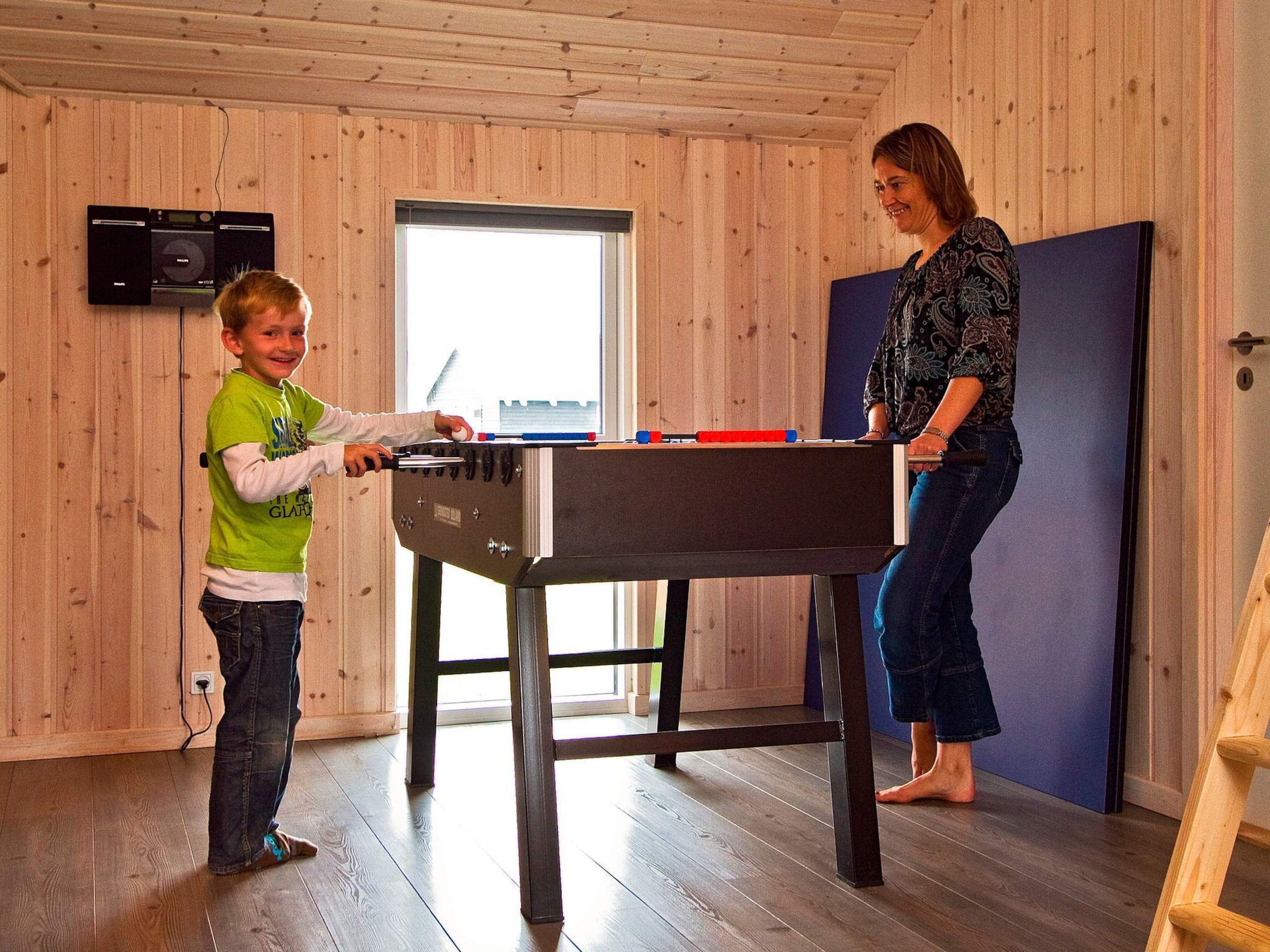 A wooden-paneled room with a foosball table and a television mounted on the wall.