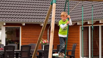 A child playing on a wooden swing set in a residential outdoor area with a tiled roof and wooden walls.