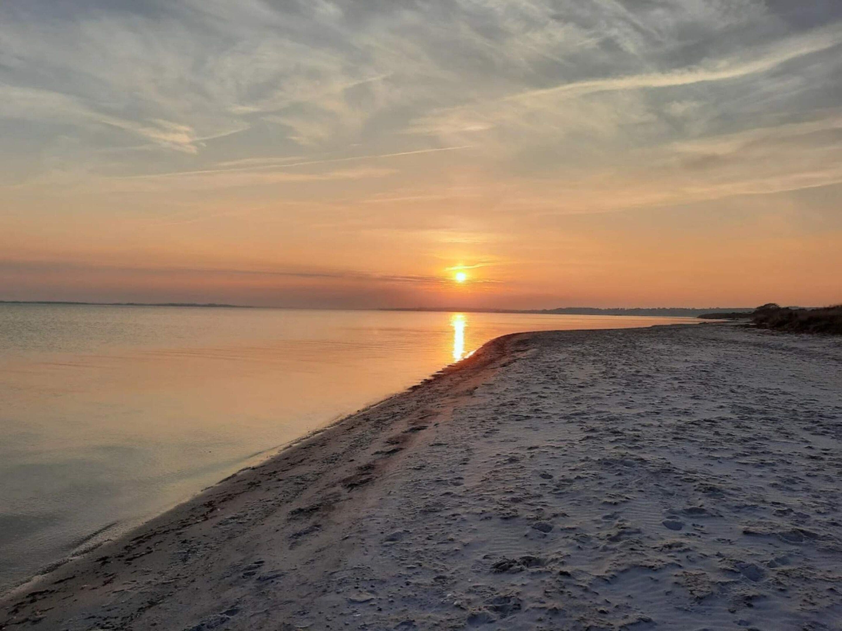 A beach at sunset with a calm sea and a clear sky.