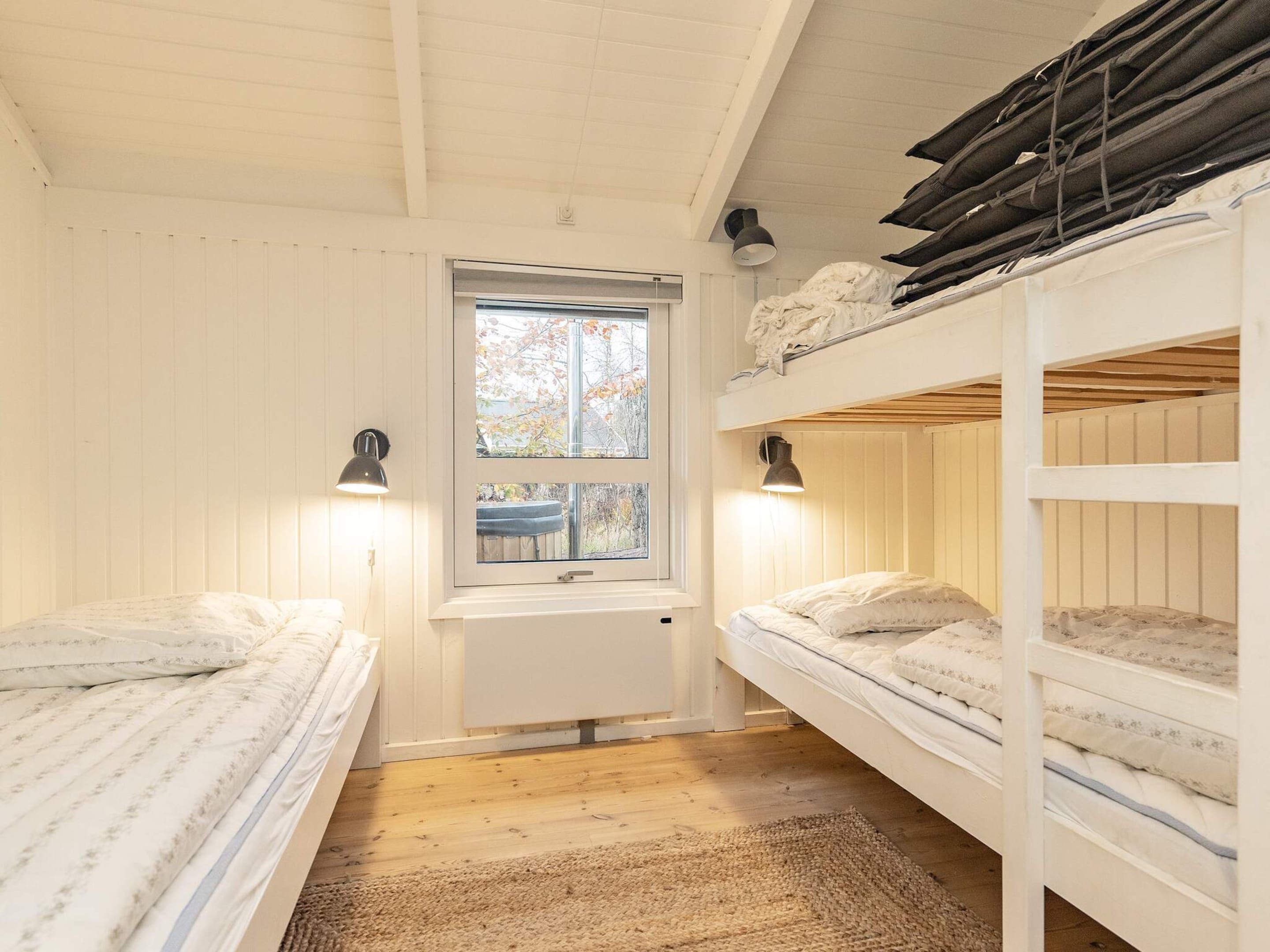 A compact room with two bunk beds, a window with a view of trees, and a small sink.