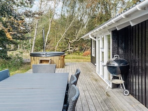 An outdoor deck with a wooden table and chairs, a hot tub, and a barbecue grill.