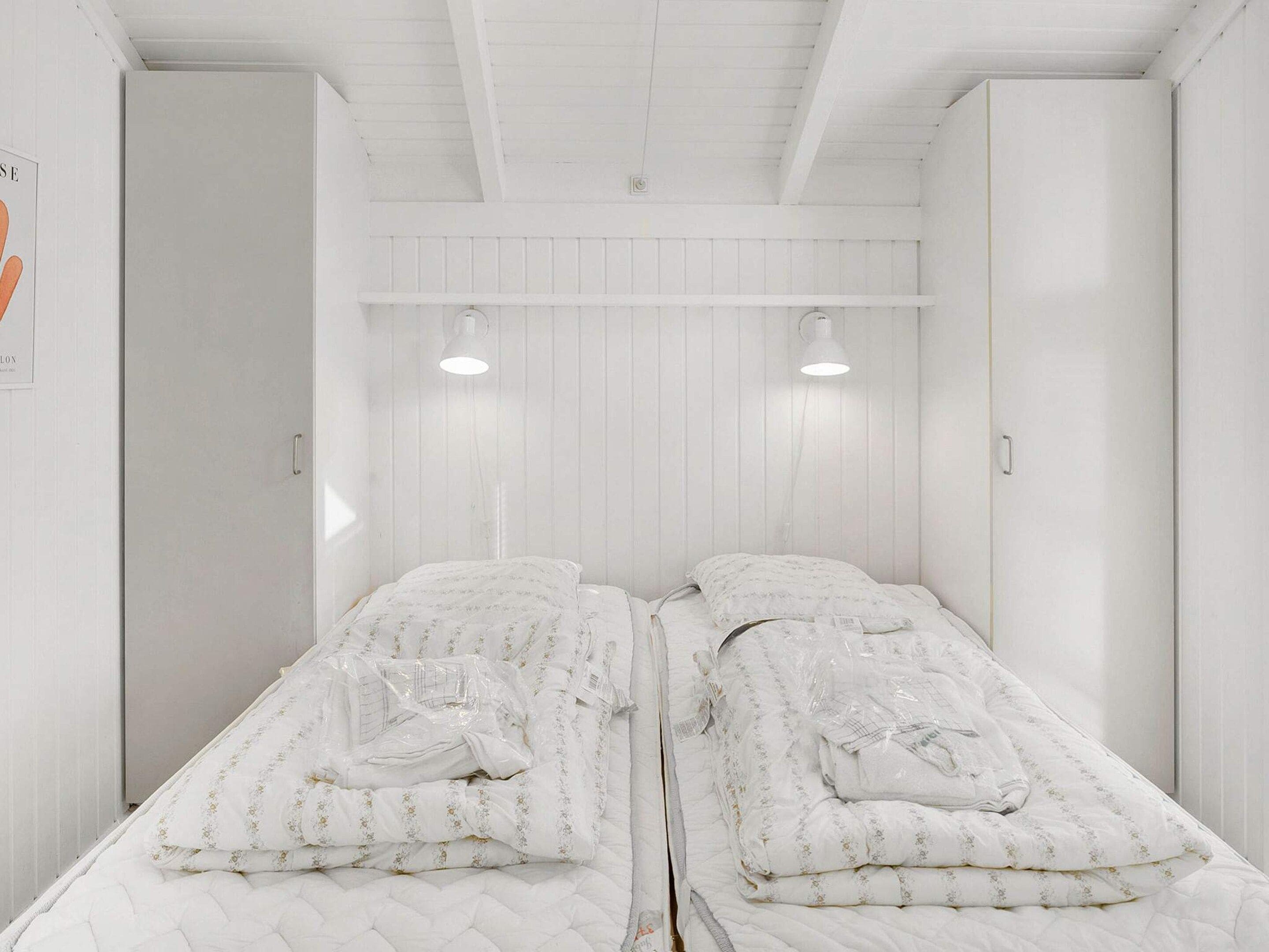 A room with two beds, each with a quilted mattress and floral bedding, white walls, and a sloped ceiling.