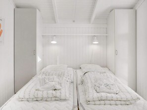 A room with two beds, each with a quilted mattress and floral bedding, white walls, and a sloped ceiling. - 4 Star Holiday Home in Albaek (Aalbaek)
