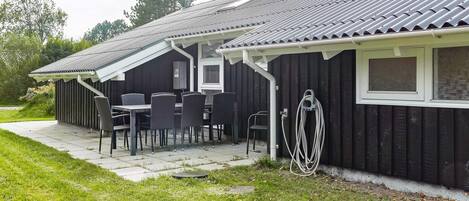 A black building with a tiled roof, a patio with chairs and a table, and a hose attached to the side.