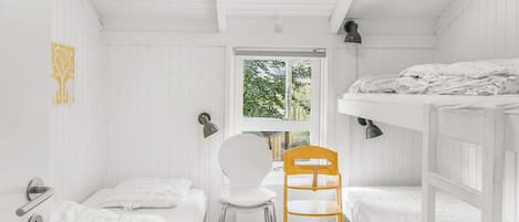 A compact room with bunk beds, a single chair, a window, and a door.