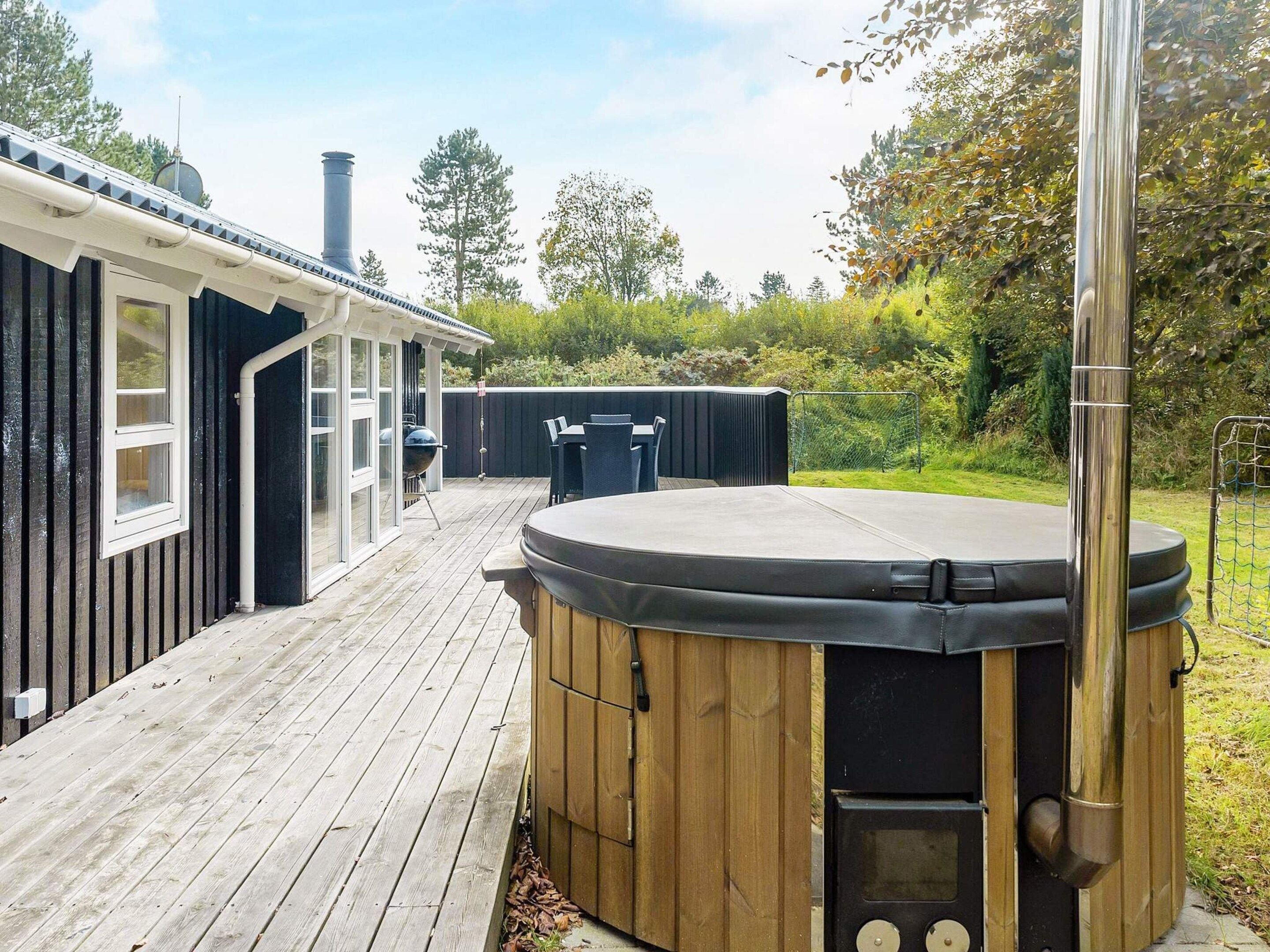 Eine Holzterrasse mit Whirlpool, Gartenmöbeln und Grill.