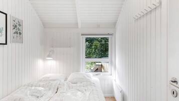 A room with two beds, a window with a view of greenery, and a white lamp.