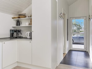 A modern kitchen with white cabinetry, a coffee maker, a kettle, and a shelf with decorative items. - 5 Star Holiday Home in Idestrup (Idestrup)