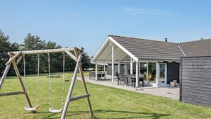 A modern house with a covered patio, a swing set, and a lawn. - 5 Star Holiday Home in Idestrup (Idestrup)