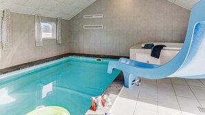 An indoor swimming pool with a blue slide, a small window, and a white cabinet with towels. - 5 Star Holiday Home in Idestrup (Idestrup)