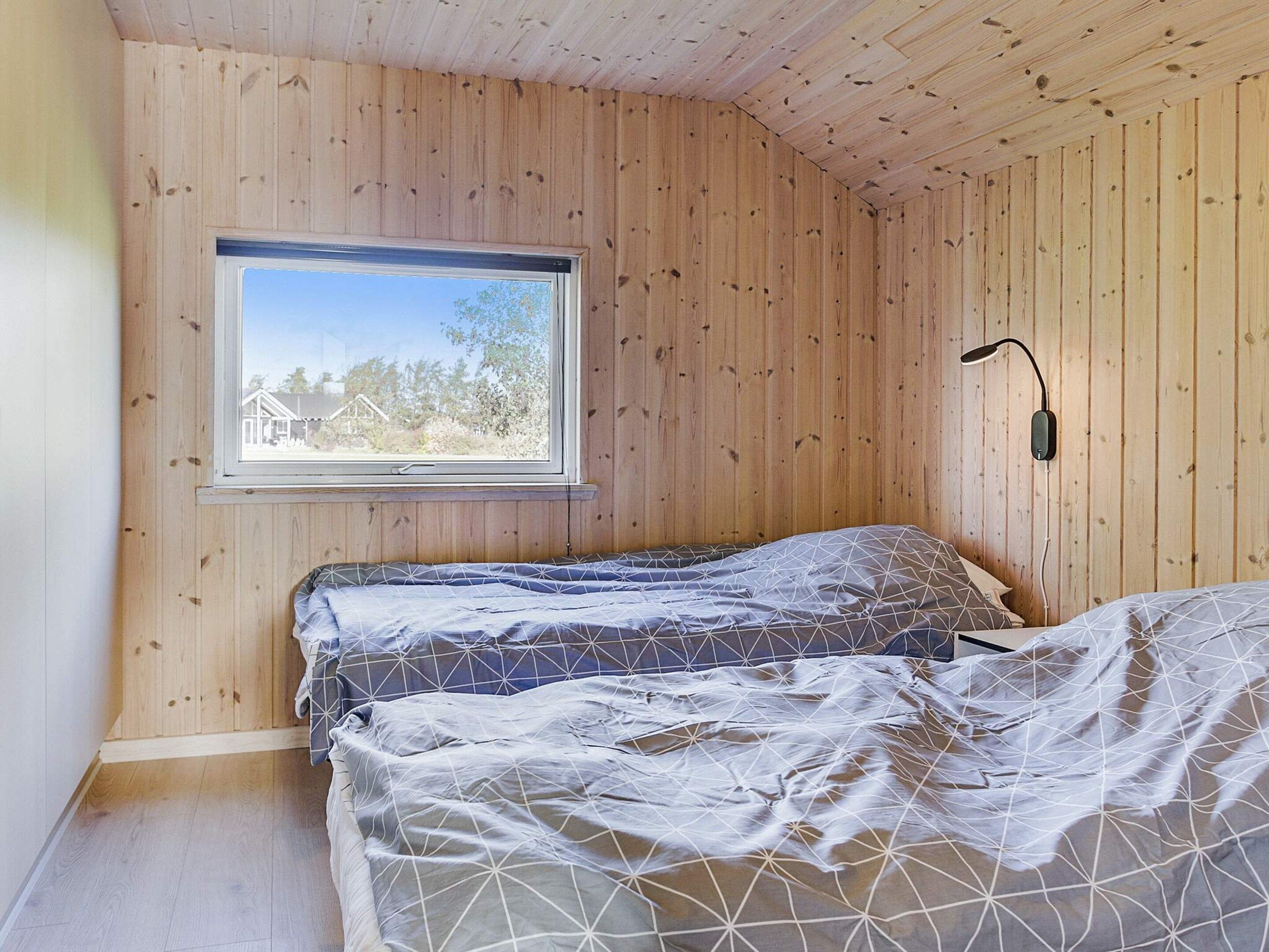 A room with wooden walls, a window with a view of houses, and a bed with patterned bedding.