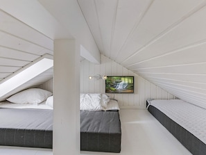 A bedroom with a sloped ceiling, a bed with white bedding, a gray bench, and a wall-mounted TV displaying a waterfall scene.