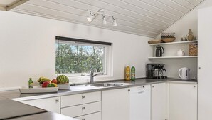 A modern kitchen with white cabinets, a stainless steel countertop, a window with a view of trees, and various kitchen appliances.