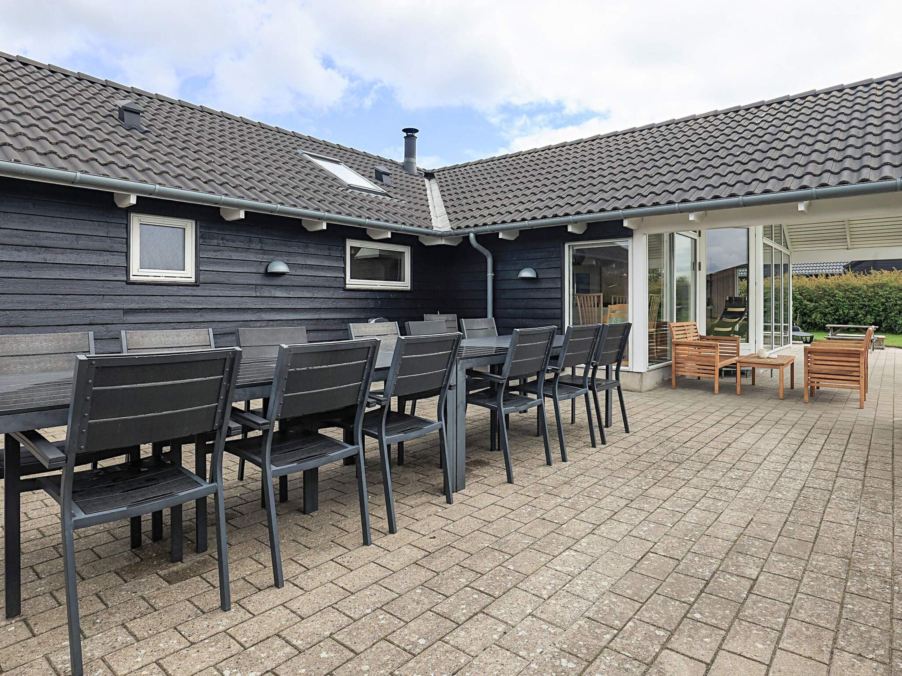 A covered outdoor patio with a dining table and chairs, a wooden deck, and a building with a tiled roof.