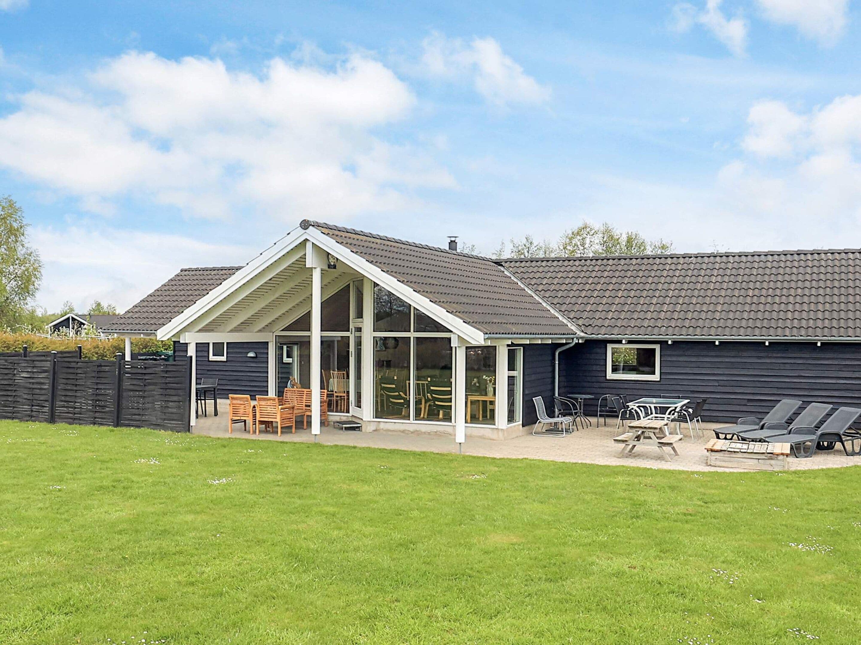 A modern house with a covered patio, a fenced yard, and outdoor furniture.
