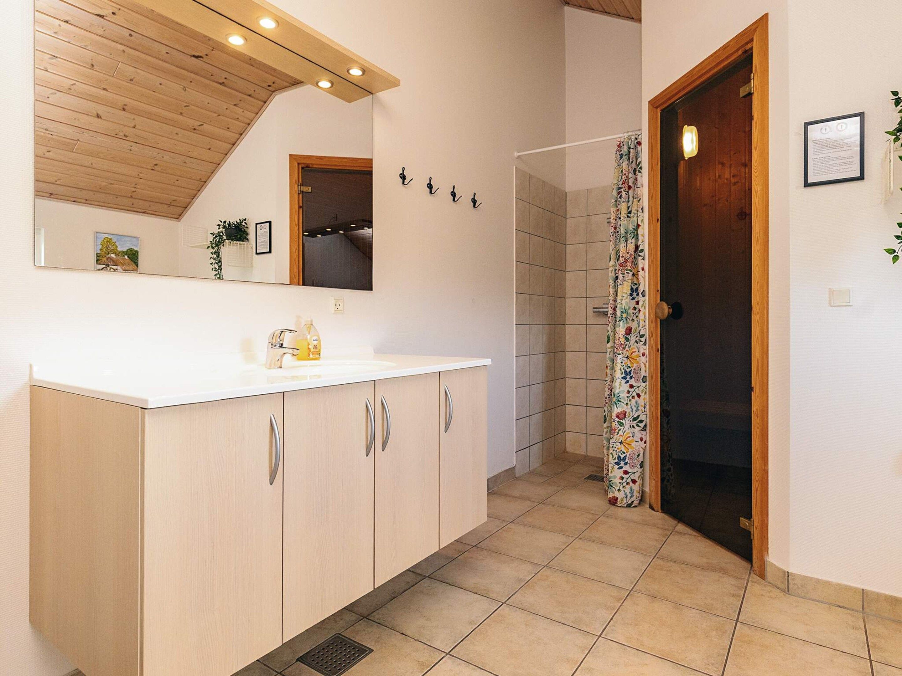 Un baño con lavamanos blanco, armarios de madera, ducha con cortina floral y techo de madera.