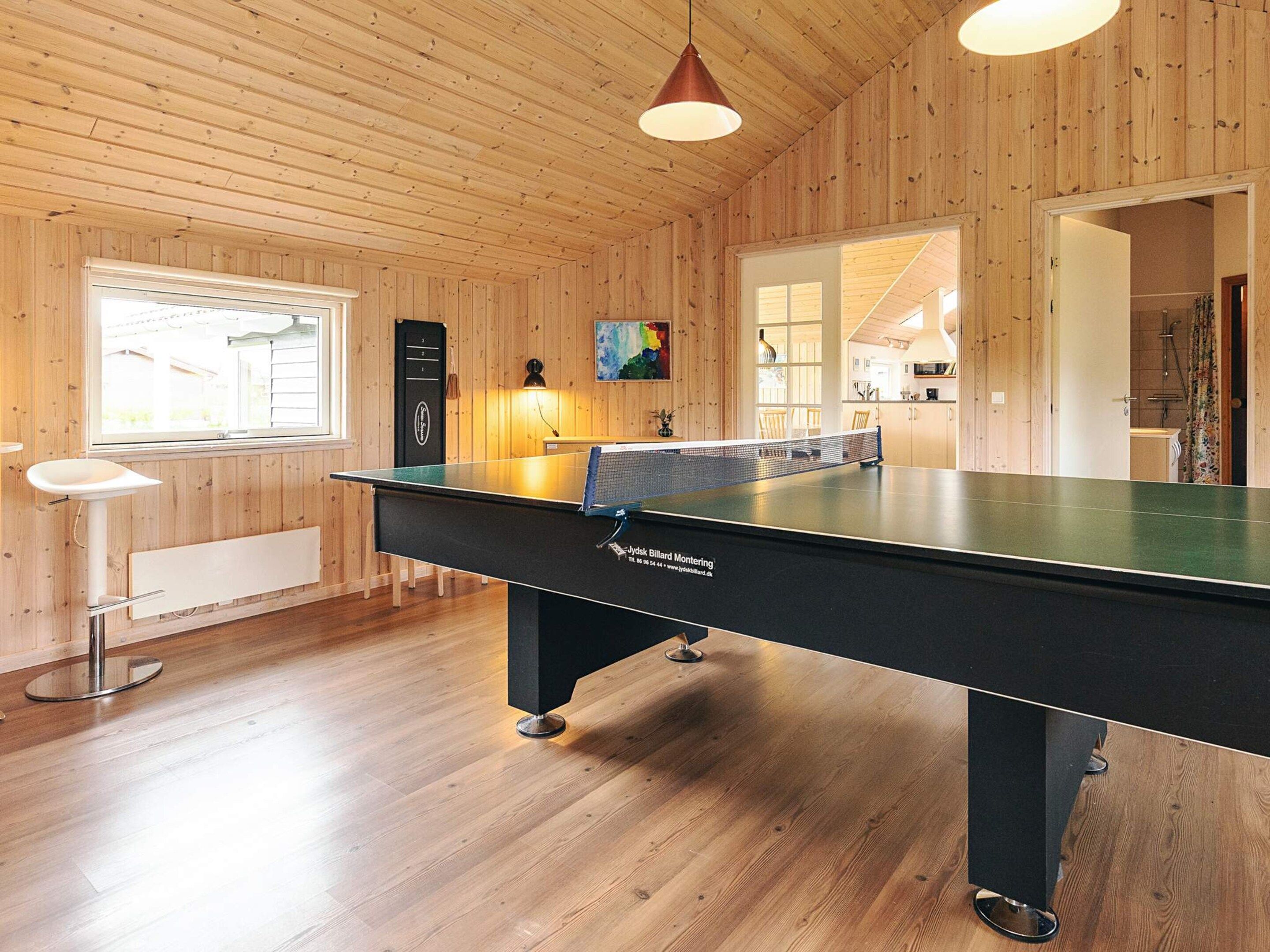 A room with a pool table, wooden walls, a window, and a door leading to a bathroom.