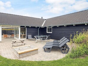 A covered patio area with outdoor furniture, including a table and chairs, and a wooden bench. - 4 Star Holiday Home in Idestrup (Idestrup)