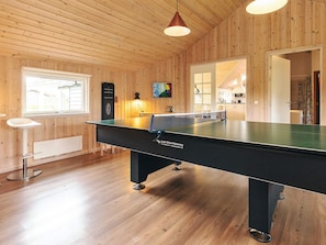A room with a pool table, wooden walls, a window, and a door leading to a kitchen. - 4 Star Holiday Home in Idestrup (Idestrup)