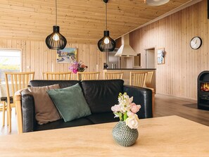 A cozy living area with a black leather sofa, wooden dining table, and a vase with flowers.