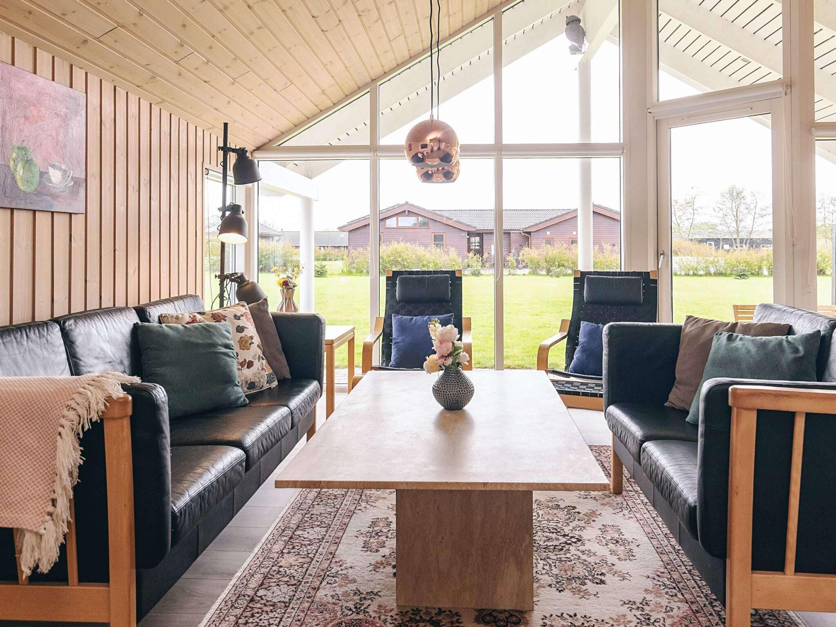 Una sala de estar moderna con techo de madera, ventanas grandes y vista a una casa.