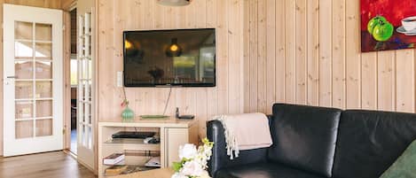 Una sala de estar con un sofá de cuero negro, una mesa de centro de madera con un jarrón de flores, un televisor de pantalla plana montado en la pared y paneles de madera en las paredes.
