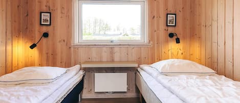 Una habitación con dos camas, paredes de madera, un ventanal y dos lámparas fijadas a la pared.