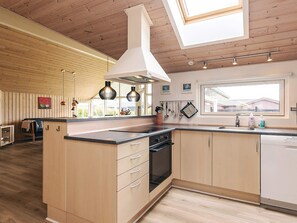 A modern kitchen with wooden cabinetry, a central island with drawers, a built-in oven, and pendant lighting. - 4 Star Holiday Home in Idestrup (Idestrup)