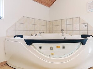 A white hot tub with two faucets and a control panel, set against a tiled wall with a wooden ceiling. - 4 Star Holiday Home in Idestrup (Idestrup)