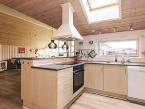 A modern kitchen with wooden cabinets, a central island with a stove, and pendant lighting. - 4 Star Holiday Home in Idestrup (Idestrup)